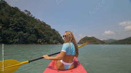 Sportive woman rows pink plastic canoe along sea water.