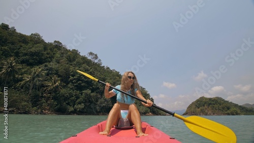 Sportive woman rows pink plastic canoe along sea water. Positive sports girl hand padding on kayak, front view. © ivandanru