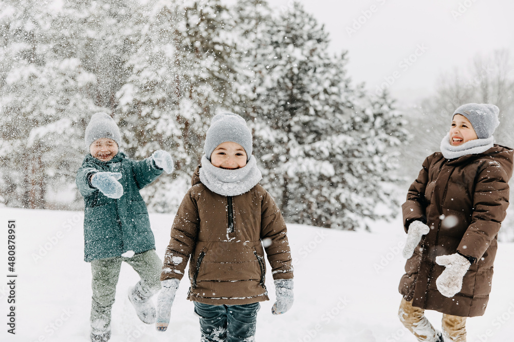 Children playing outdoors on a snowy winter day in a forest, laughing, having fun.