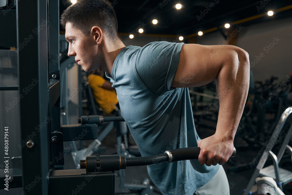 Concentrated sportsman doing strength-training exercise on fitness machine Concentrated sportsman doing strength-training exercise on fitness machine