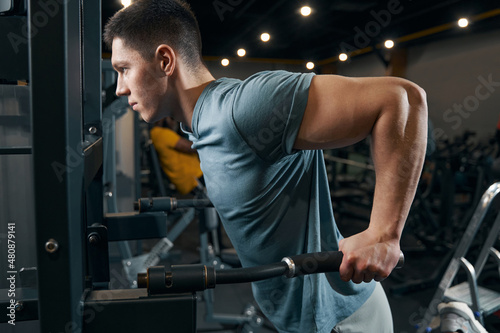 Concentrated sportsman doing strength-training exercise on fitness machine