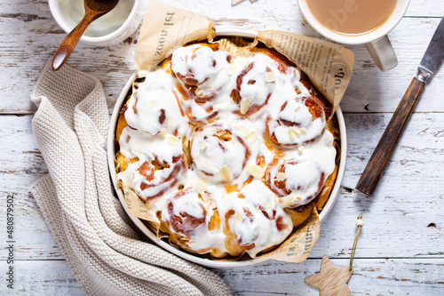 Cinnabons in a round bowl with curd cream on a wooden table, top view, horizontal