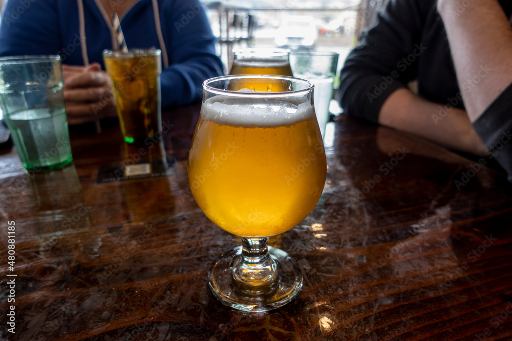 View of a frothy, ice cold farmhouse ale on a wooden table inside a restaurant View of a frothy, ice cold farmhouse ale on a wooden table inside a restaurant