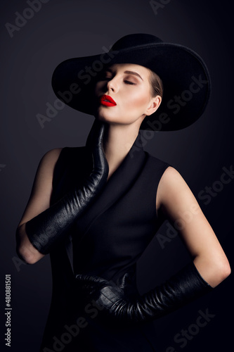 Fashion Beauty Woman Portrait in Hat with Red Lips Make up. Elegant Old fashioned Lady in Gloves dreaming with Closed Eyes over Black Studio Background photo