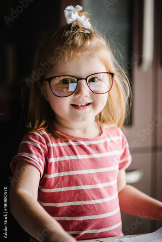 Happy small blonde girl looking in camera with happy and peaceful expression in brand new glasses.