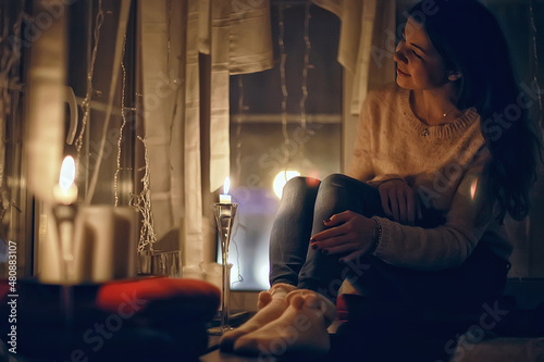 girl at the window dreams in winter evening / the romance of candle, the beautiful model in Christmas evening dreams