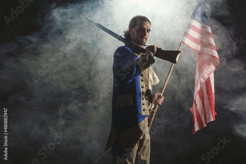 Billede på lærred American revolution war soldier with flag of colonies and musket gun over dramatic smoke background