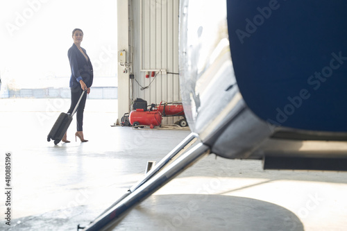 Elegant lady with trolley suitcase standing in aircraft hangar photo