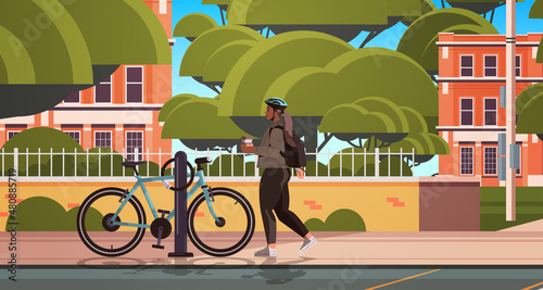 female cyclist taking break during bike ride woman in helmet with takeaway coffee cup standing near bicycle