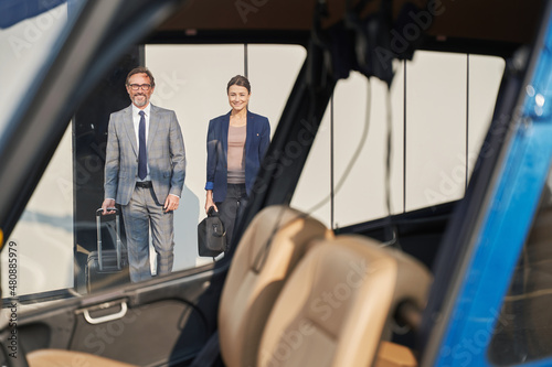 Two smiling businesspeople with baggage approaching helicopter