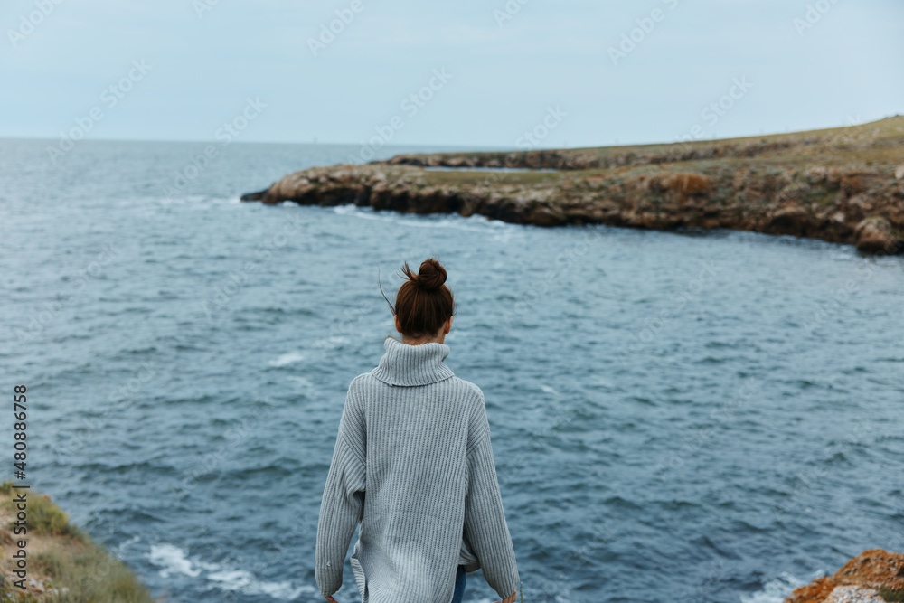 woman in a gray sweater stands on a rocky shore nature Relaxation concept