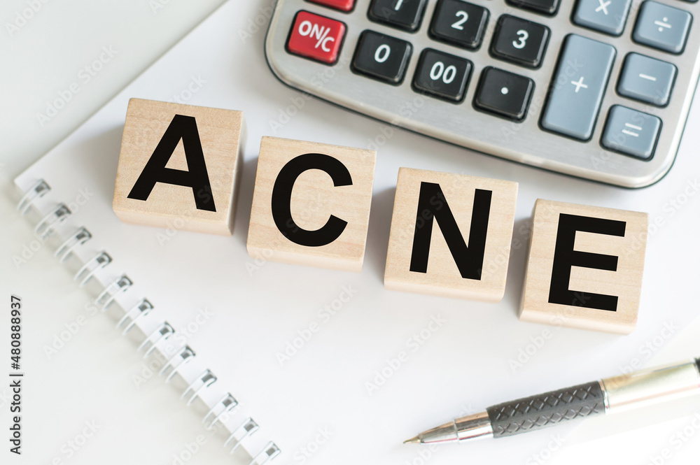 Medicine concept. ACNE word on wooden cubes on a table next to a notebook, calculator and pen Medicine concept. ACNE word on wooden cubes on a table next to a notebook, calculator and pen