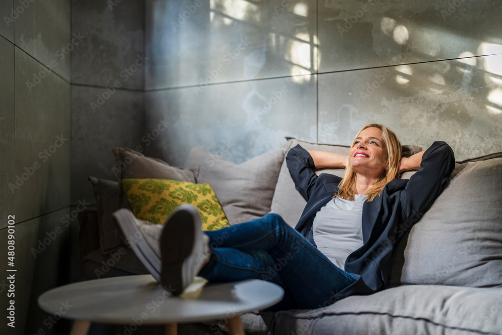 Businesswoman relaxing with hands behind head on sofa at office Businesswoman relaxing with hands behind head on sofa at office