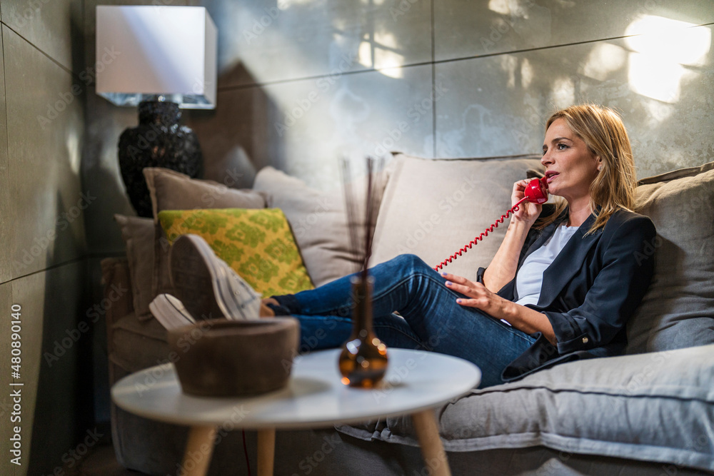 Businesswoman talking through landline phone sitting on sofa at office