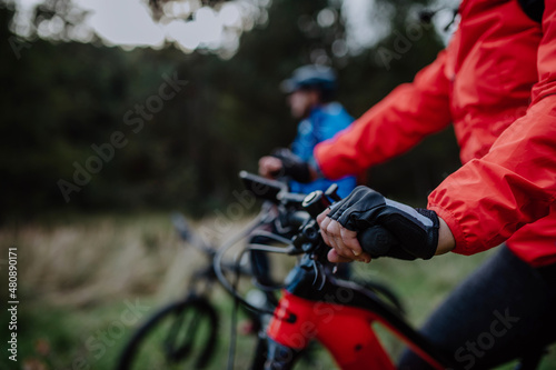 Detail of senior woman's hand riding bikes outdoors with her husband in forest in autumn day.