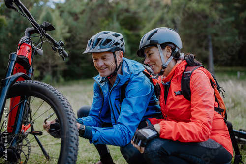 Active senior couple mending bicycle outdoors in forest in autumn day.