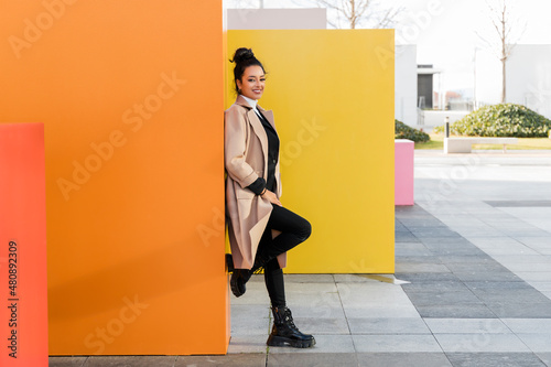 Smiling businesswoman leaning on orange wall