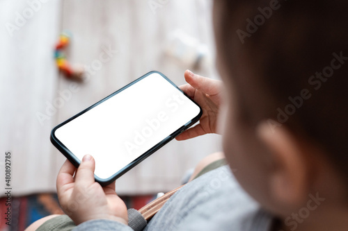 Boy's toddler hands holdingphone on home background. Child's hands hold black smartphone and watching video in horizontal position. Screen blank. Close-Up. photo