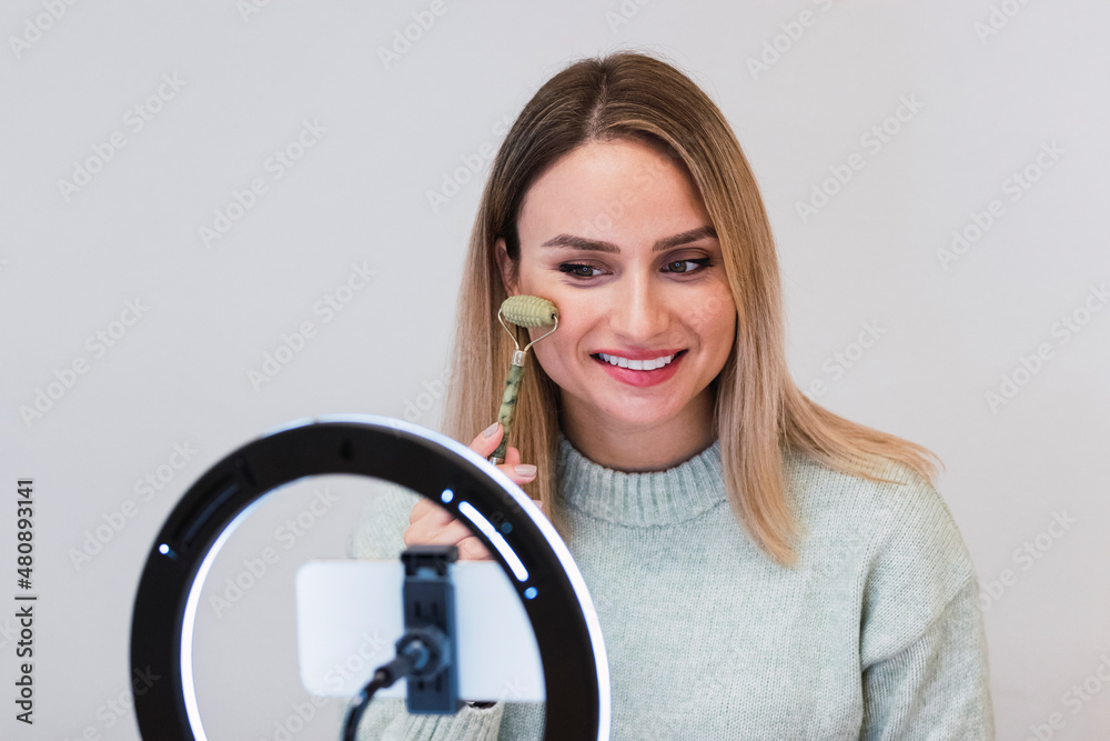 Smiling influencer filming tutorial with jade roller in front of ring light Smiling influencer filming tutorial with jade roller in front of ring light