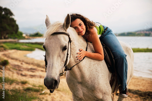 Smiling woman lying on horse at waterfront at sunset photo