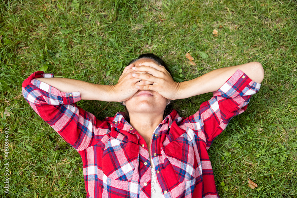 Woman covering eyes with hands lying on grass Woman covering eyes with hands lying on grass