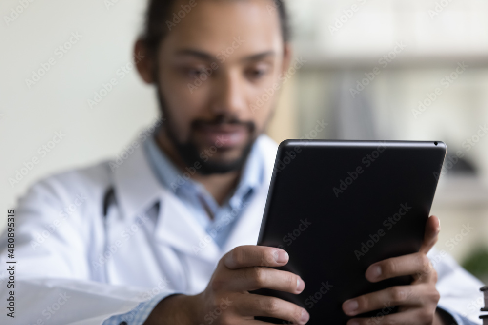 Close up focus on digital touchpad gadget in hands of young male African American general practitioner doctor physician, medical healthcare application usage, modern tech devices in telemedicine. Close up focus on digital touchpad gadget in hands of young male African American general practitioner doctor physician, medical healthcare application usage, modern tech devices in telemedicine.