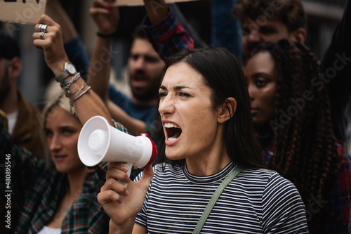Young woman manifesting marching on a protest shouting into a megaphone photo