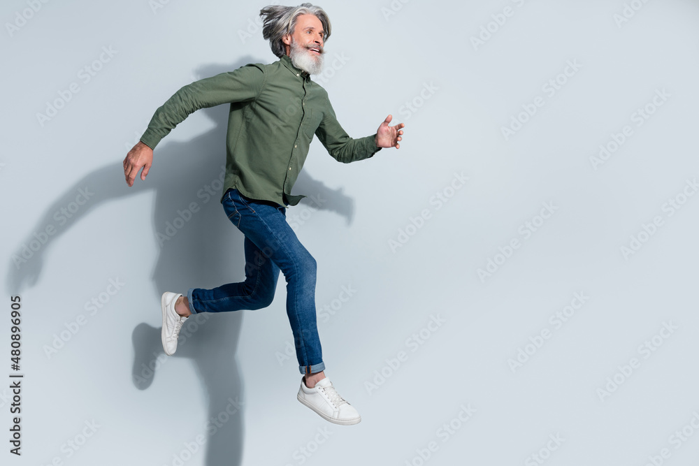 Photo of handsome man pensioner dressed khaki shirt running empty space jumping high isolated grey color background