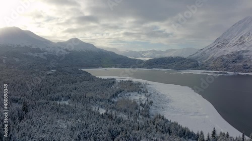 Aerial orbit of an Alaskan sunrise over Snowy Mountain. An untouched lake surrounded by a snow covered forest sits below the mountain. photo