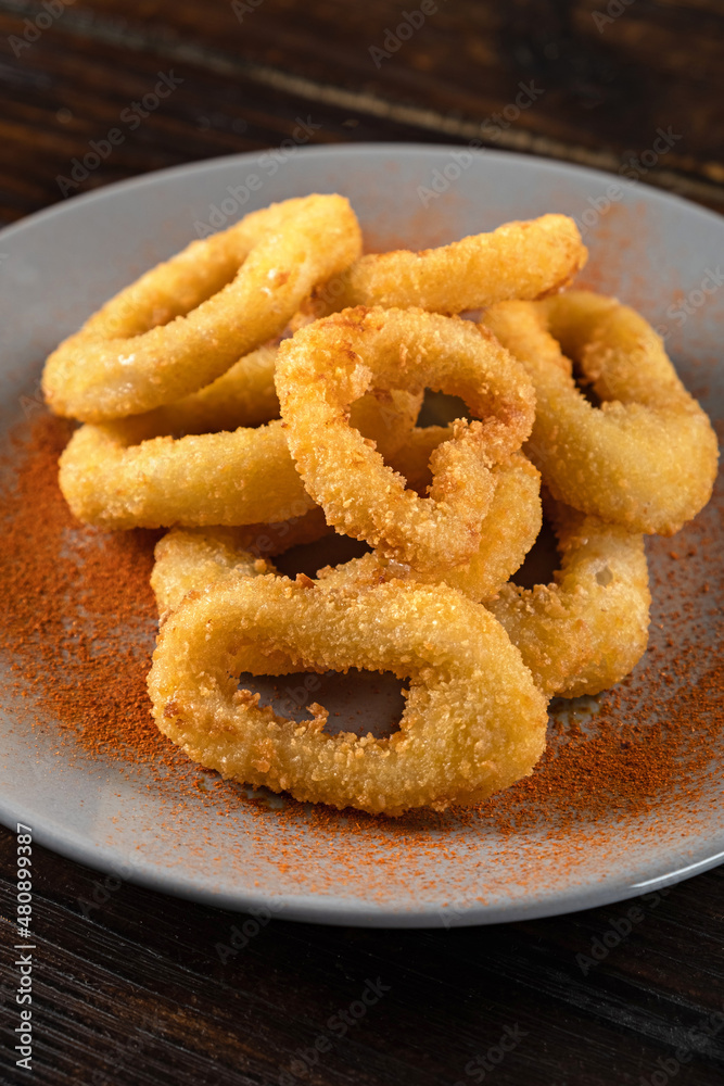Beer appetizer from squid rings in batter in a plate on a wooden table. Vertical orientation, close-up, dark moody Beer appetizer from squid rings in batter in a plate on a wooden table. Vertical orientation, close-up, dark moody