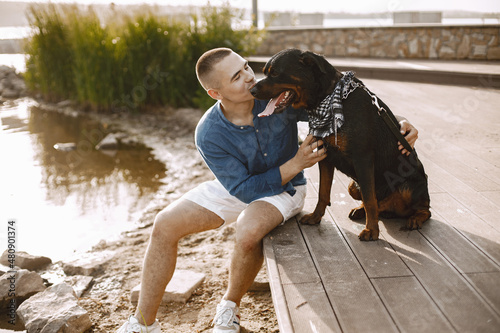 Man with rotweiller dog sitting together near the lake