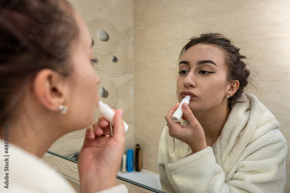 beautiful young girl in a white coat makes a boring makeup to a spacious mirror. beautiful young girl in a white coat makes a boring makeup to a spacious mirror.