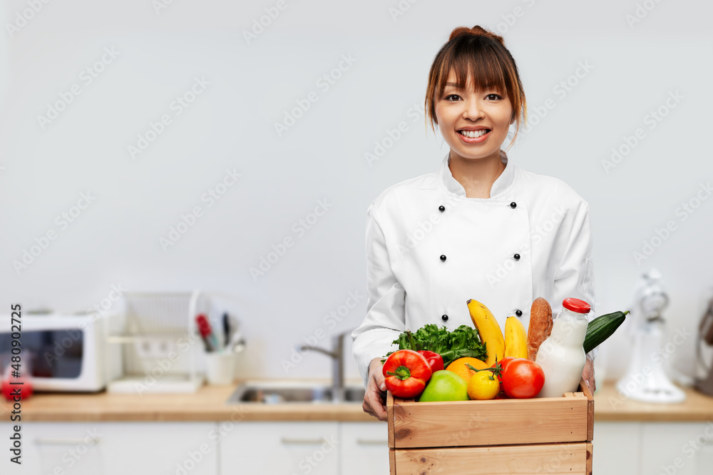 cooking, culinary and people concept - happy smiling female chef in toque holding food in wooden box over restaurant kitchen background