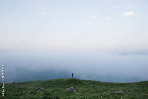 Tiny Human in mountainous area against background of field of grass and clouds. man alone with nature. little man in big world