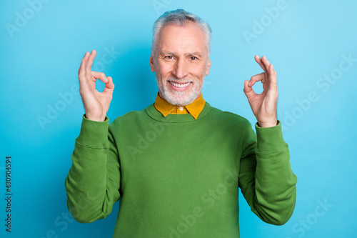 Photo of pretty handsome retired man wear green sweater showing two okey gestures isolated blue color background