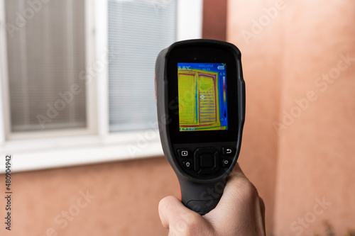 A male hand holds a thermal imager at the window of a house. Search for heat loss in private houses photo