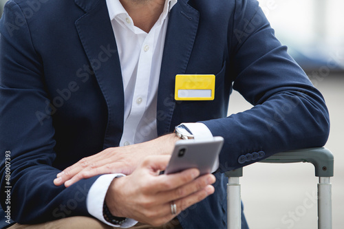 Close up of business man sitting on street with suitcase luggage and using a smartphone 