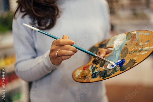 Closeup picture of a woman, holding a long paint brush and carefully applying colors.