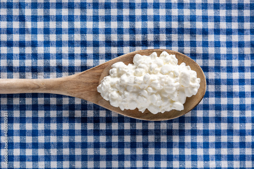Fresh cottage cheese in wooden spoon on blue tablecloth