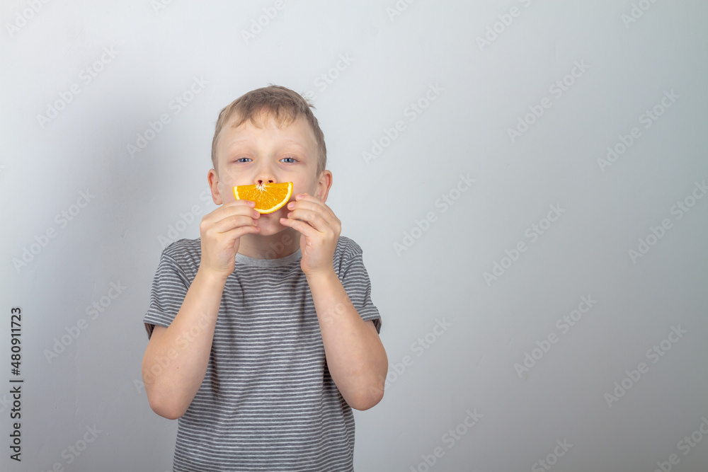 Cheerful caucasian boy smiles made a smile from a slice of orange on a gray background Cheerful caucasian boy smiles made a smile from a slice of orange on a gray background