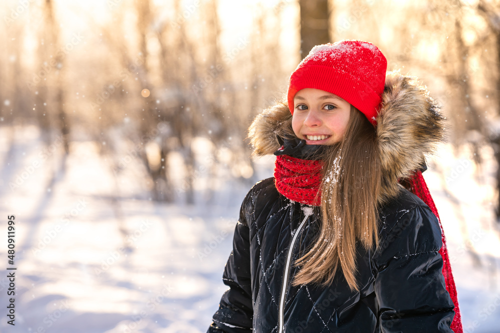 Portrait of a charming little girl in a red hat in a snowy forest in winter. Christmas winter holidays. Happy childhood