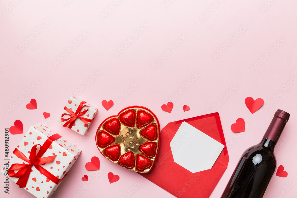 Bottle of red wine on colored background for Valentine Day with gift box, envelope and chocolate. Heart shaped with gift box of chocolates top view with copy space