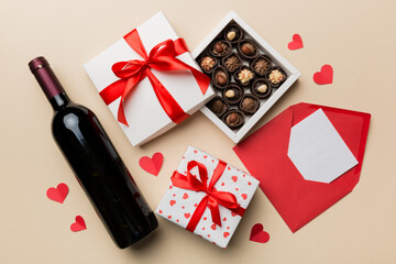 Bottle of red wine on colored background for Valentine Day with gift box, envelope and chocolate. Heart shaped with gift box of chocolates top view with copy space