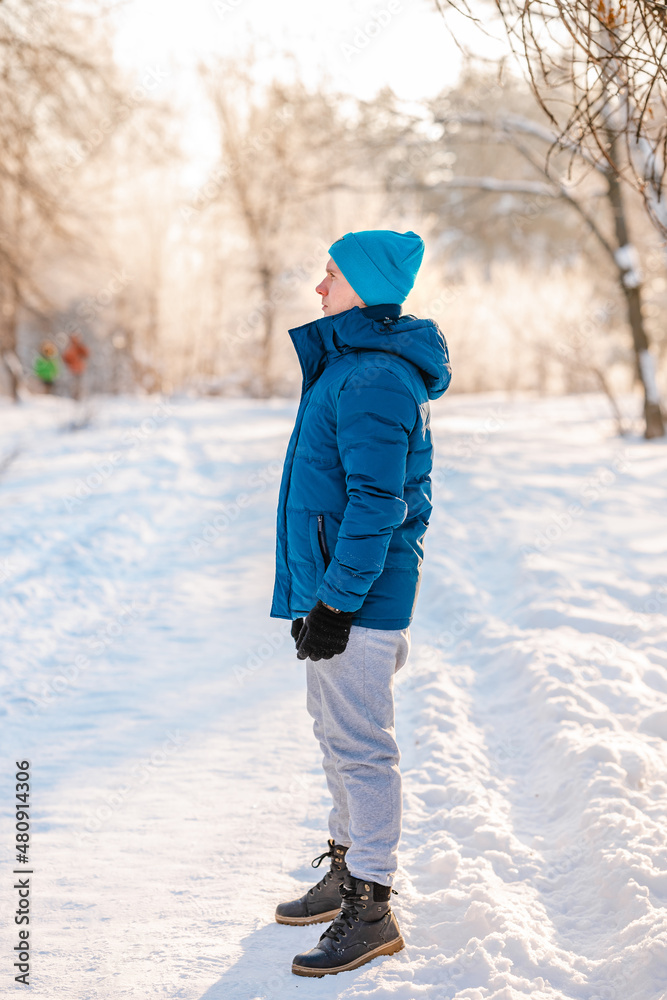 A young man in a blue jacket stands on a path in a snowy winter forest