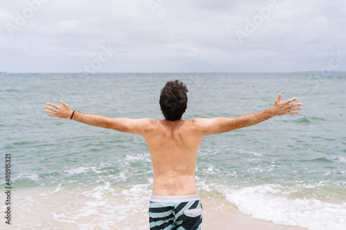 Full length image of unrecognizable man on tropical island seashore with raised arms. Panoramic rear view of man in swim suit on paradisiacal beach. People traveling and holidays concept © beavera