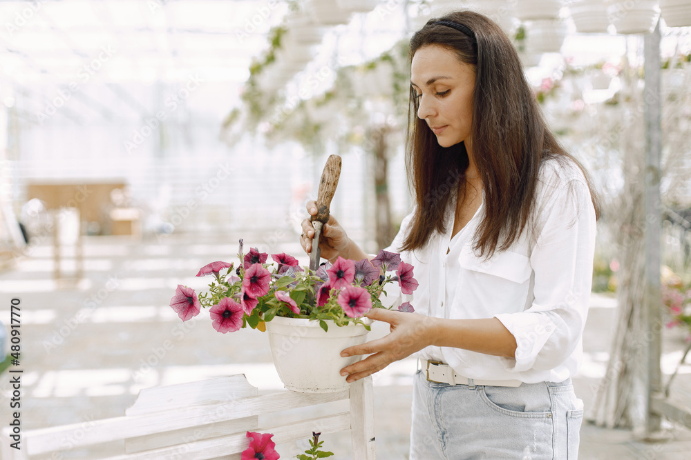 Side view of female gardener inspecting potted flowers in greenhouse Side view of female gardener inspecting potted flowers in greenhouse