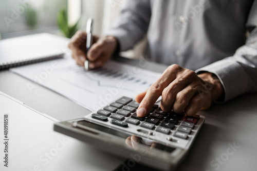 Accountant calculate finance report using calculator and holding document closeup, business man working in finance accounting and analyze financial budget in office