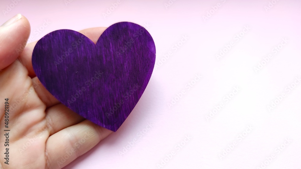 Fototapeta premium Hand holds a purple heart. Expression of understanding and compassionate love. Love and caring. The concept of parents and children. Military medal for wounded soldiers.