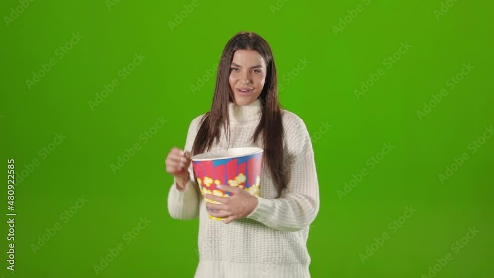 Positive caucasian woman in white knitted sweater dancing with basket of tasty popcorn while enjoying new film. Chroma key background in studio. Positive caucasian woman in white knitted sweater dancing with basket of tasty popcorn while enjoying new film. Chroma key background in studio.