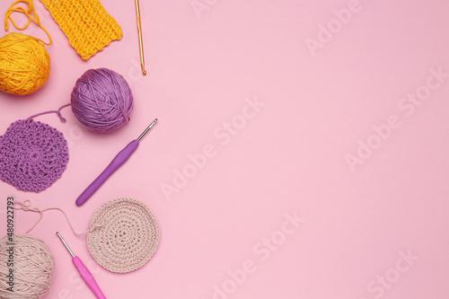 Flat lay composition with knitting threads and crochet hooks on pink background, space for text